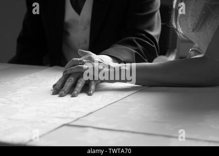 Weibliche Braut und männlicher Bräutigam Brautpaar hält die Hände auf dem Tisch Zeigt Eheringe in schwarz-weiß mit Kopierraum Stockfoto