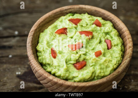 Guacamole mit Stücken von Tomaten in eine Schüssel auf rustikalen Holztisch Stockfoto