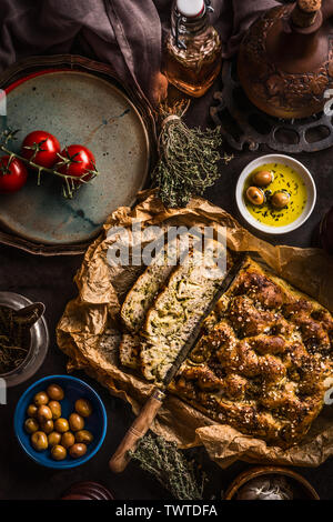 In Scheiben geschnitten hausgemachten focaccia Brot und Messer mit Olivenöl und Oliven auf rustikalen Tabelle, Ansicht von oben. Italienisches Essen Konzept.