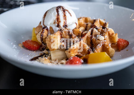 Waffeln mit Eis bedeckt Schokolade und mit Obst auf einem Teller auf den Tisch eingerichtet. Stockfoto