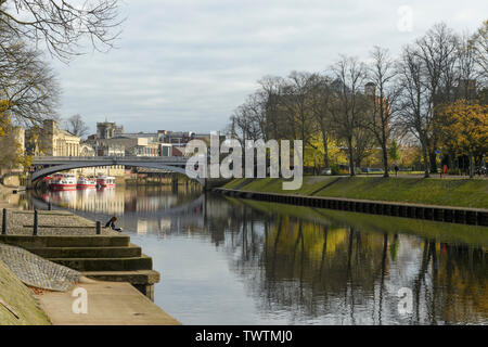 Ruhigen malerischen Lage am Fluss von Lendal Brücke (Bäume im Fluss Ouse & Frau Lesung wider am Ufer) - York, North Yorkshire, England, UK. Stockfoto