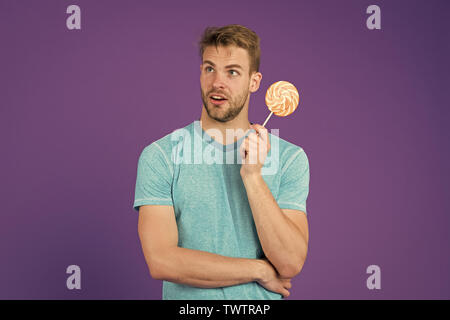 Cheat meal Konzept. Zucker schädlich für die Gesundheit. Kerl halten Lollipop candy violett unterlegt. Mann schöner macho Essen großen bunten süßen Lutscher. Geschmack der Kindheit. Mann mit Borsten mag Lollipop. Stockfoto