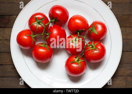 Blick von oben auf die roten gewaschene Tomaten auf große weiße Platte auf dem Holztisch. Wassertropfen auf frischen sonnengereiften Gemüse. Eiche dunkel Tabelle. Gesunde Ernährung Menü Stockfoto