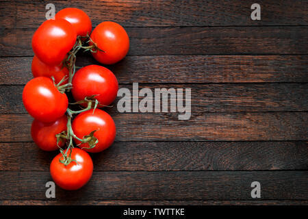 Frische rote Tomaten am Zweig auf dunkle braune Eiche Tisch. Kopieren Sie Platz. Holz Textur verbrannt. Ansicht von oben. Horizontale Ausrichtung. Linke Stellung bringen. Stockfoto