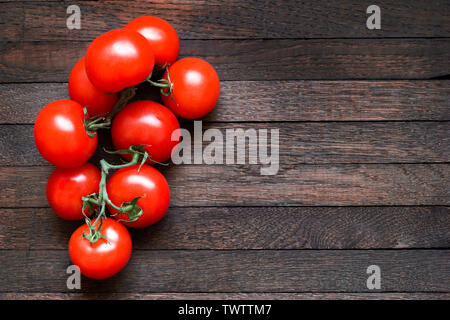 Frische rote Tomaten am Zweig auf dunkelbraunen hölzernen Tisch. Eiche Textur. Ansicht von oben. Kopieren Sie Platz. Horizontale Ausrichtung. Linke Stellung bringen. Stockfoto