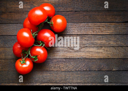 Frische rote Tomaten am Zweig auf dunkelbraunen hölzernen Tisch. Kopieren Sie Platz. Eiche Textur. Ansicht von oben. Horizontale Ausrichtung. Linke Stellung bringen. Stockfoto