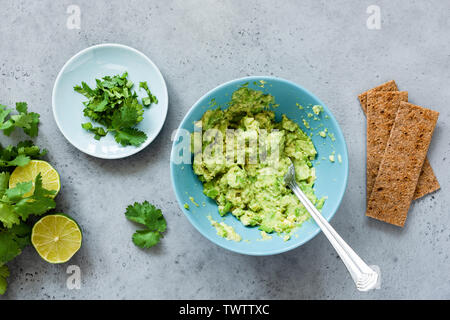 Guacamole in der Schüssel und Roggen Knäckebrote. Die Guacamole Sauce, gesunde Vegetarische Vorspeise oder Snack. Ansicht von oben Stockfoto