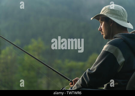 Junge Mann in einem Rollstuhl Angeln am schönen See, Sonnenuntergang, Dämmerung Stockfoto