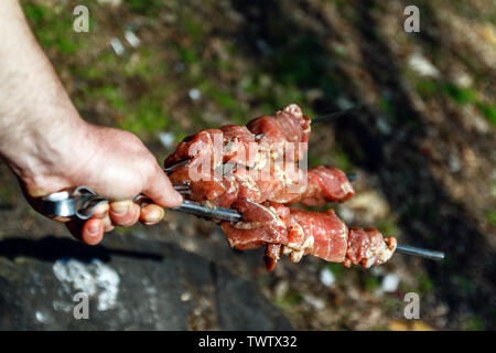 Mann hält in der Hand einen Spieß mit rohem Fleisch, Life Style. Stockfoto