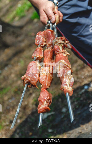 Mann hält in der Hand einen Spieß mit rohem Fleisch, Life Style. Stockfoto