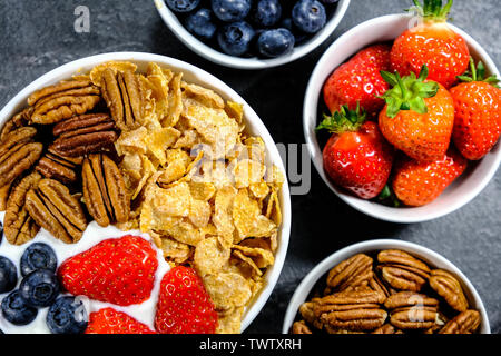 Gesundes Frühstück mit Müsli mit frischem Obst und Nüsse, Corn Flakes, Pecan Nüsse, Erdbeeren, Heidelbeeren und Joghurt. Stockfoto