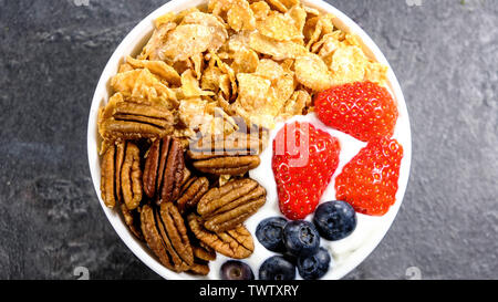 Gesundes Frühstück mit Müsli mit frischem Obst und Nüsse, Corn Flakes, Pecan Nüsse, Erdbeeren, Heidelbeeren und Joghurt. Stockfoto