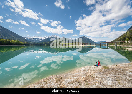 Frau sitzt am Ufer des Sylvenstein Stausee und das Karwendelgebirge im türkisfarbenen Wasser, Bayern reflektiert suchen, Deutschland Stockfoto