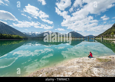 Frau sitzt am Ufer des Sylvenstein Stausee und das Karwendelgebirge im türkisfarbenen Wasser, Bayern reflektiert suchen, Deutschland Stockfoto