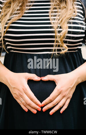 Eine schwangere Frau, die in einem schwarz-weiss gestreiftes Kleid mit langen blonden Haaren Stockfoto