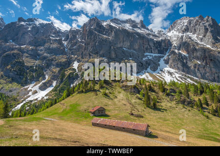 Imposante Bergmassiv ragt über Almen und Schutzhütten im Tal unten. Gefahrenstellen Skipisten in den Dolomiten. Üppigen Weide. Stockfoto