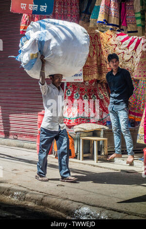 Mann, der ein enormes Paket auf seinen Kopf auf einer Geschäftsstraße in Old Delhi, New Delhi, Indien Stockfoto