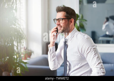 Close-up Portraitfotos der stattlichen Geschäftsmann mit Hemd und Krawatte im Büro sitzt und spricht mit jemand auf seinem Handy. Stockfoto