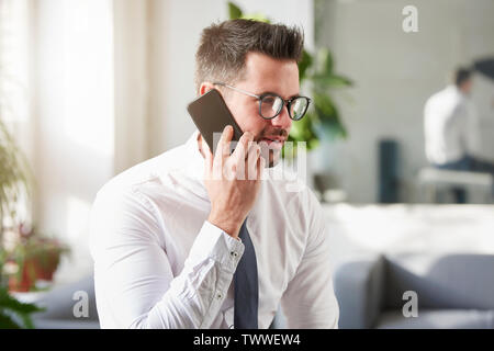 Close-up Portraitfotos der stattlichen Geschäftsmann mit Hemd und Krawatte im Büro sitzt und spricht mit jemand auf seinem Handy. Stockfoto
