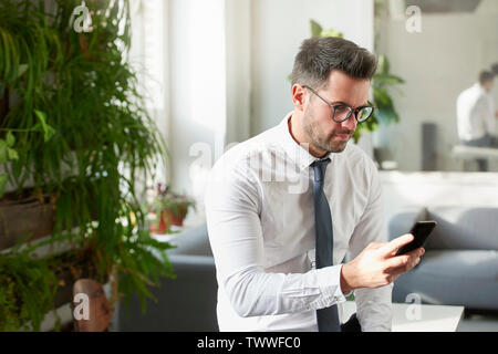 Portraitfotos der Geschäftsmann mit seinem Handy und Sms, während im Büro zu sitzen. Stockfoto