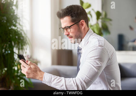 Portraitfotos der Geschäftsmann mit seinem Handy und Sms, während im Büro zu sitzen. Stockfoto