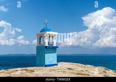 Traditionelle griechische kleine Kirche oder Kapelle. Blauer Himmel mit weißen Wolken und Meer im Hintergrund Stockfoto