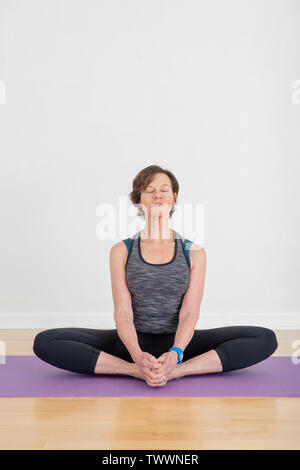 Eine 70 Jahre alte Yoga Lehrer in ihrem Studio ist eine Hip opener Pose namens Gebunden Winkel darstellen, aka Baddha Konasana Stockfoto