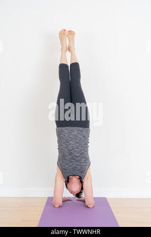 Salamba Sarvangasana, Shoulderstand mit einer Wand für die Unterstützung von einem 70 Jahre alten Yoga Instructor gemacht. Von der Seite gesehen. Stockfoto