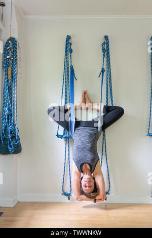 Eine 70-jährige Weiblich Yoga Lehrer in ihrem Studio ist eine umgekehrte Asana mit Wand Seile, aka Yoga kurunta, Stockfoto