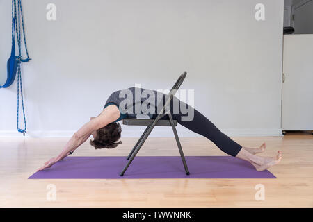 Eine 70 Jahre alte Frau Yoga Lehrer in ihrem Studio zeigt Iyengar Yoga Stuhl Backbend Stockfoto