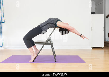 Eine 70 Jahre alte Frau Yoga Lehrer in ihrem Studio zeigt Iyengar Yoga Stuhl Backbend Stockfoto