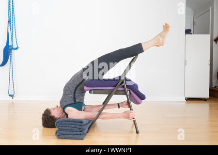 Eine 70 Jahre alte Frau Yoga Lehrer in ihrem Studio zeigt Iyengar Yoga Stuhl Backbend Stockfoto