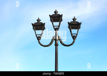 Foto von drei modernen Metall Lampen im Vintage Stil auf einem einzigen Post vor blauem Himmel Stockfoto