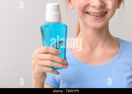 Smiling teenage Mädchen mit Zahnspangen holding Flasche Mundspülung auf grauem Hintergrund Stockfoto