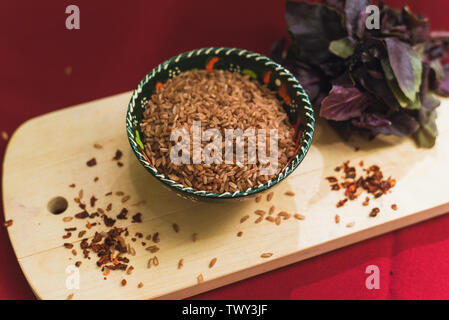 Zira Reis liegt in einem orientalischen Platte. dunklen Reis liegt auf einem orientalischen Hintergrund, eine goldene Tischdecke, einem hölzernen Schneidebrett neben Basilikum. Vorbereitung für das Kochen Pilav. Stockfoto