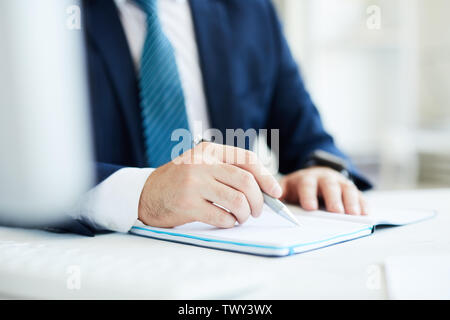 Nahaufnahme der unkenntlich Geschäftsmann in Anzug sitzt am Schreibtisch und Kontrolle der Noten im Tagebuch beim Denken an Geschäftsziele Stockfoto