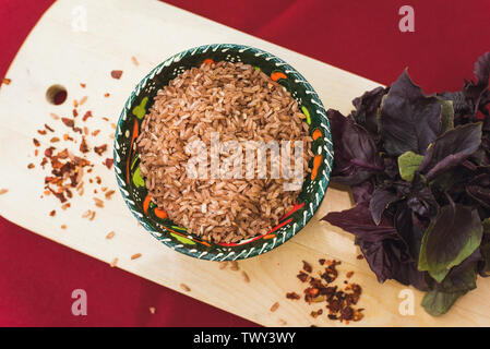 Zira Reis liegt in einem orientalischen Platte. dunklen Reis liegt auf einem orientalischen Hintergrund, eine goldene Tischdecke, einem hölzernen Schneidebrett neben Basilikum. Vorbereitung für das Kochen Pilav. Stockfoto