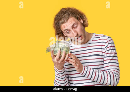 Emotionale Mann hält Glas mit Geld auf farbigen Hintergrund Stockfoto