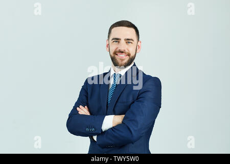 Portrait von lächelnden Erfolgreiche bärtigen Geschäftsmann in Anzug gegen weiße Wand und verschränkte die Arme Stockfoto