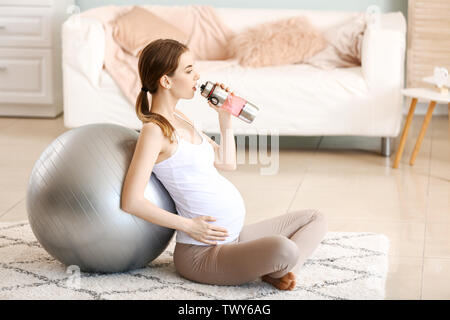 Schöne schwangere Frau Trinkwasser beim Training zu Hause Stockfoto