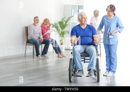 Junge Betreuer nach deaktiviert reifer Mann im Pflegeheim suchen Stockfoto