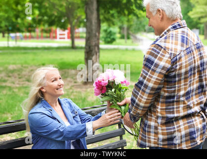 Reife Frau Blumen von ihrem Ehemann in Park Stockfoto