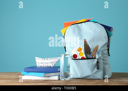 Rucksack mit Schulmaterial auf hölzernen Tisch gegen Farbe Hintergrund Stockfoto