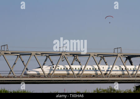 Ein Parapenter fliegt über eine Brücke, während ein shinkansen (Hochgeschwindigkeitszug) der Serie N700 vorbeifährt. Kurami, Kanagawa, Japan. Stockfoto