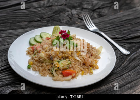 Gebratener Reis mit Garnelen und Gemüse in einem weißen Teller auf einen alten Holztisch, aus der Nähe. Thailändische Küche, thailändische Küche. Gebratener Reis mit Meeresfrüchten in der Res Stockfoto