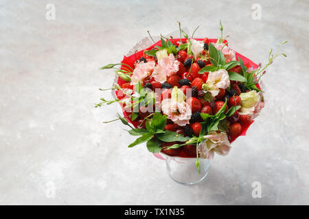 Einzigartige Strauß Blumen, Erdbeeren, Kirschen und Brombeeren steht in einer Vase auf einem Marmortisch Stockfoto