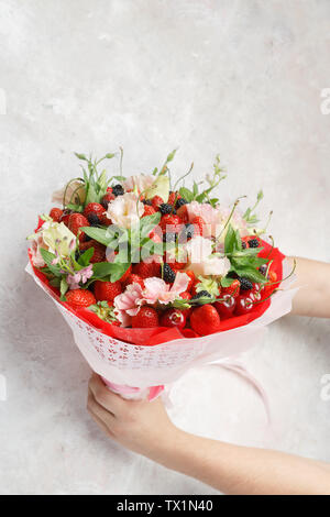 Einzigartige Strauß Blumen, Erdbeeren, Kirschen und Brombeeren in den Händen von Männern auf einem Marmor Hintergrund Stockfoto