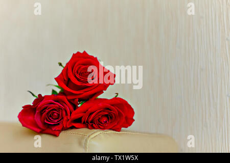 Drei rote Rosen liegen auf einem beigen Hintergrund. Die Fokussierung auf die in der Nähe von Rose. Close-up. Kopieren Sie Platz. Stockfoto