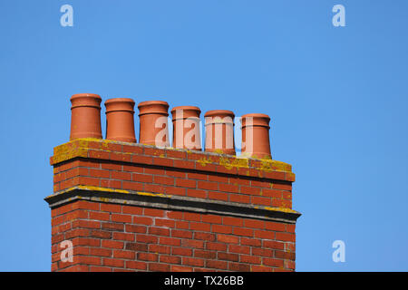 Viktorianische rot terracotta Ton Schornstein Töpfe auf einem roten Lehm gemauerten Schornstein montiert vor blauem Himmel gezeigt. In Cardiff, Wales, Großbritannien Stockfoto