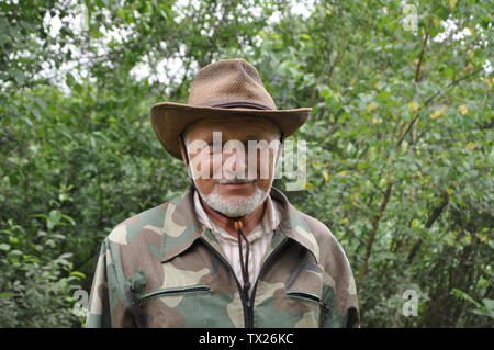 Reisenden mittleren Alters. Porträt einer stattlichen erwachsenen Mann mit grauem Bart und Hut in Camouflage Kleidung vor dem Hintergrund des Waldes Stockfoto